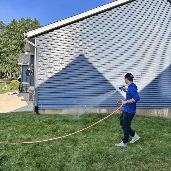 Soft washing the side of a house with a wide low-pressure spray.