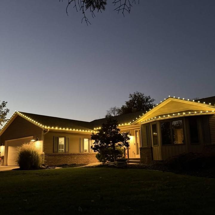 A house at dusk with warm string lights along the roofline.