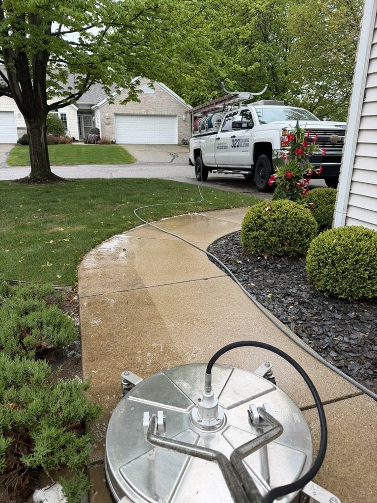 A surface cleaner part-way along the walk from the drive to a front door, cleaned concrete behind it and the 323 truck alongside.