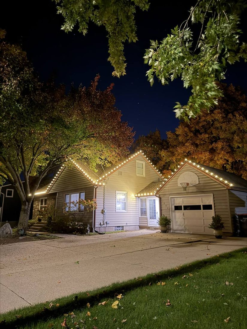 A house at dusk with warm string lights along the roofline.