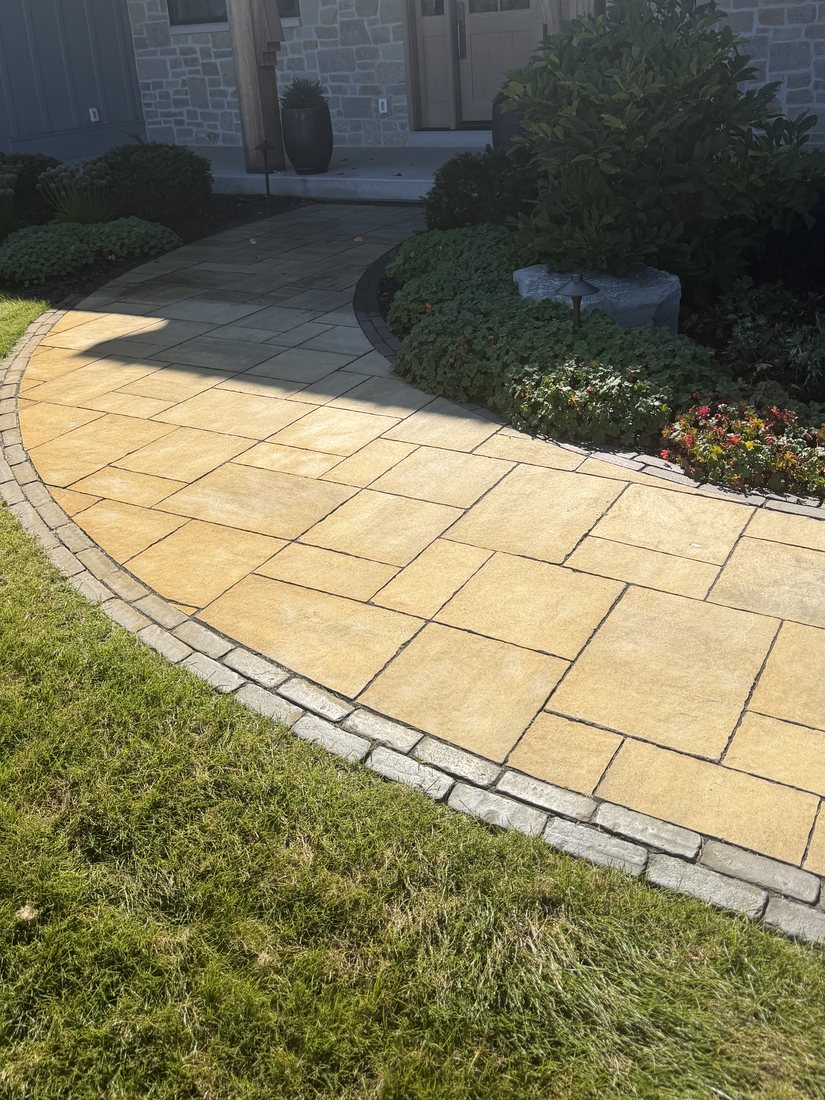 A curved paver walkway stained a uniform rust orange from the lawn edge in.