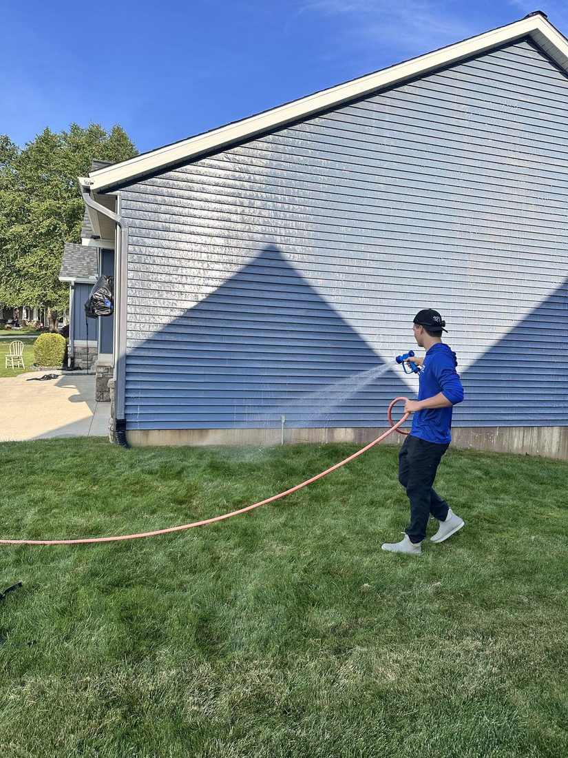 Soft washing the side of a house with a wide low-pressure spray.