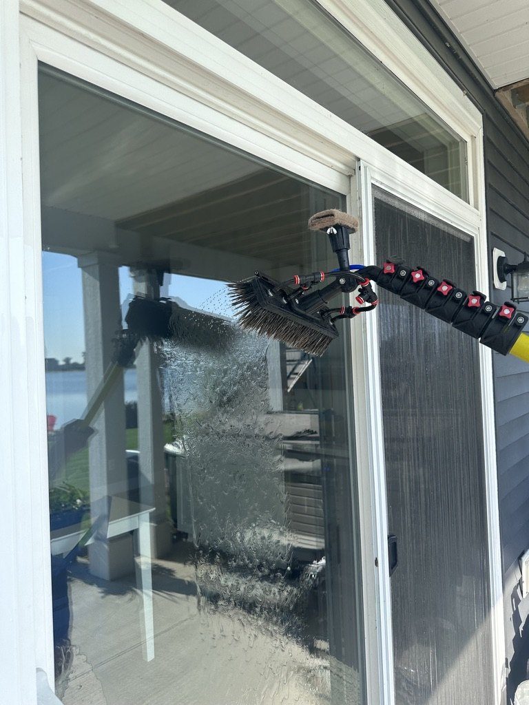 A water-fed pole brush scrubbing a sliding glass door, water running down the pane.